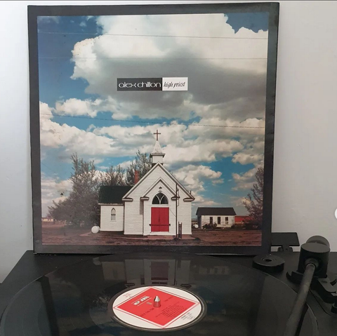 Record playing with the sleeve propped behind - sleeve shows a church under a cloudy sky - and the words "Alex Chilton - High Priest"