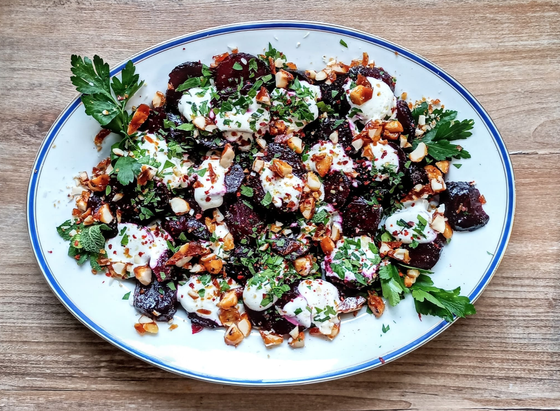 Das fertige Gericht auf einer Platte. Rote Bete mit Klecksen von Joghurt, darüber Petersilie und Nusskrokant und Chiliflocken.