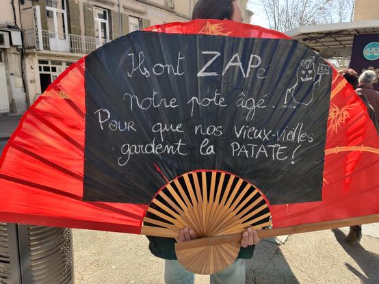 Écriteau en forme d'éventail géant sur lequel est écrit "Ils ont ZAPé notre pote agé. Pour que nos vieux/vieilles gardent la PATATE !" (En référence à la zad zone à patate de Pertuis qui a été détruite par le maire qui veut artificialiser quelques hectares de terre agricole pour son propre intérêt)