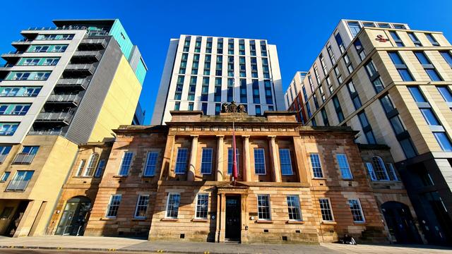 A classically designed old sandstone building surrounded by modern multi-storey office developments.