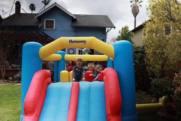 Three children play in a bounce house in the backyard.