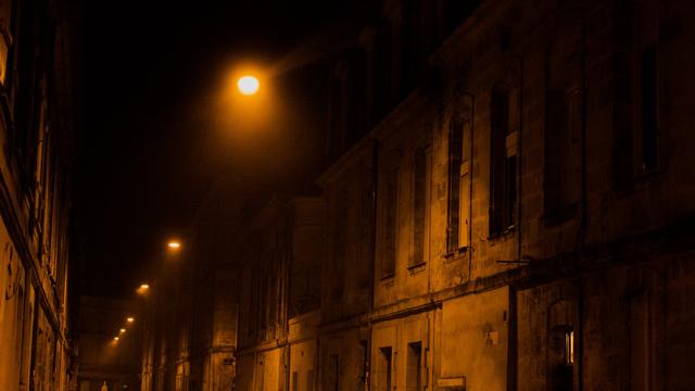 Une rue bordelaise de nuit, éclairée par l'éclairage public jaunâtre. Il y a du brouillard : la lumière est très diffusée dans ce dernier. La rue s'enfuie vers l'infini