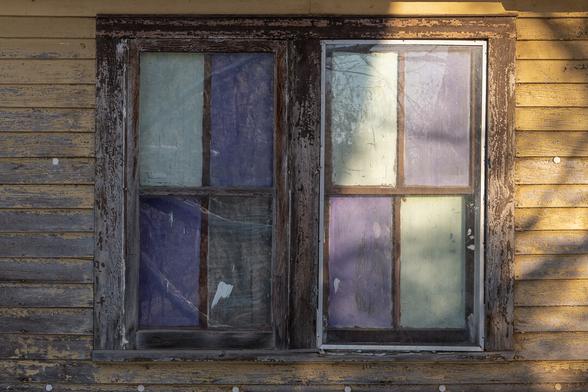 A pair of windows of an abandoned wooden farmhouse. Patchy winter light on the walls.