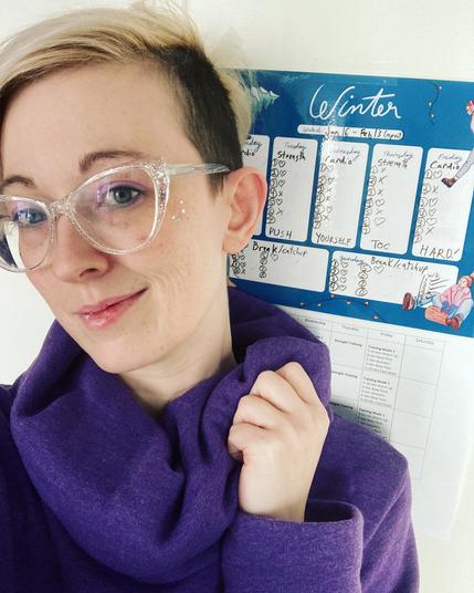 Sonja is looking tired but cute. On the wall behind them is an activity tracker sheet. Across the middle of it is written “DON’T. PUSH.YOURSELF.TOO.HARD!”