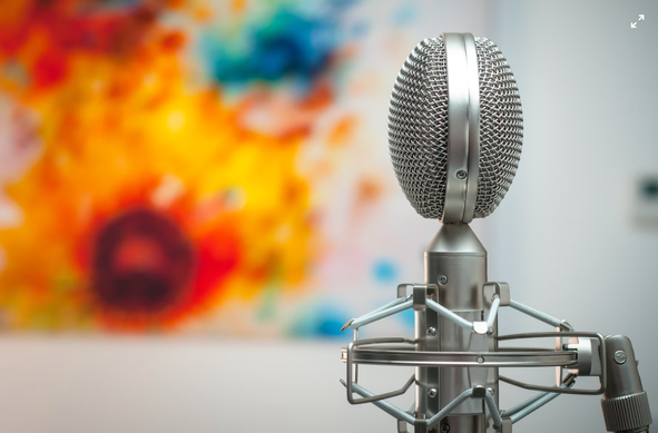 A professional silver microphone stands in sharp focus against a soft-focus, splashy, colorful background.