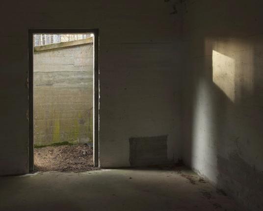 Colour horizontal photograph of the inside of a derelict WW2 bunker, with light coming in through a doorway on the left and striking the wall on the right.