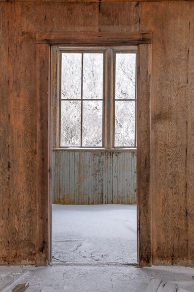 Schoolhouse interior, Very bare. a fine layer of snow lies on the ground. The wooden walls are peeling or bare wood.