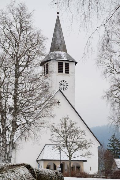 Eine weiße Kirche im Winter. Etwas Schnee liegt auf dem Dach und einem Baum links.