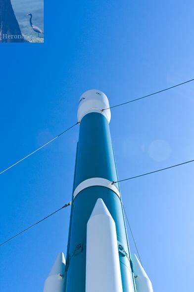 A photograph of a Delta II rocket, from a very low angle, looking up along the blue of the rocket, with the white fairing on top, and three white solid rocket boosters attached at the base.