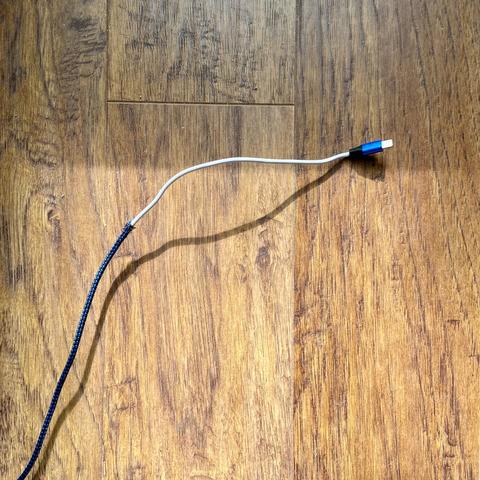 Woven black and blue fabric-covered USB cable that has been skinned alive by our cats.🤣 The white exposed portion of the cable, directly below the connector, shows the naked plastic casing after the infliction of the aforementioned critical damage, with this USB cable sustaining a total loss of negative 30 hit points.😉