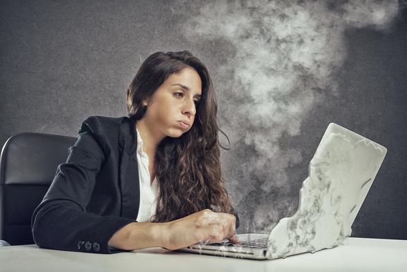Light skinned woman with long dark hair in a business jacket and white shirt with looking annoyed as her laptop literally smokes and melts in front of her - deposit photos