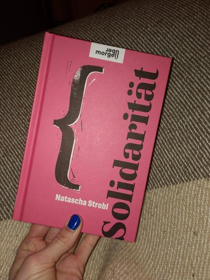 Ein rotes Buchcover mit Schwarzer Schrift: 'Solidarität' von Natascha Strobel. Mittig ist eine große schwarze geschweifte Klammer.