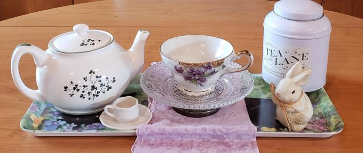A white, green and purple tea tableau with a garden theme of violets, rabbits, and shamrocks. The tea is Cinnamon black tea.
