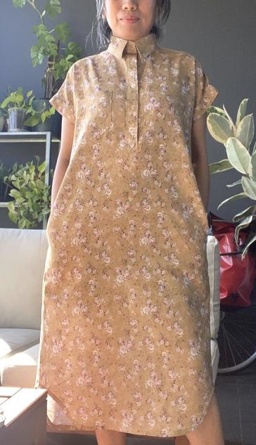 A person wearing a long shirt dress that they sewed in a yellow floral print.
