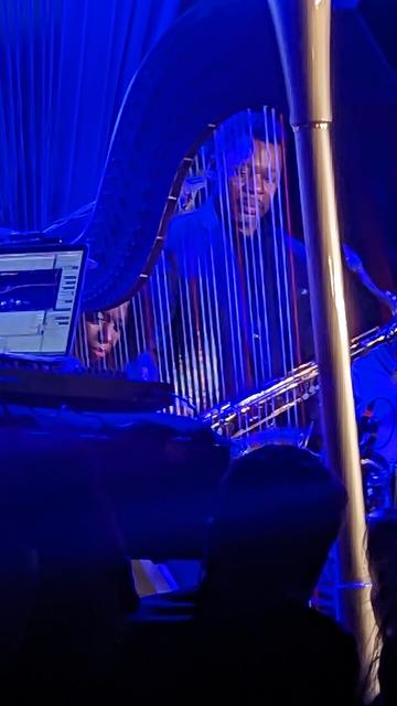 Ravi Coltrane with saxophone around his neck & watching Brandee Younger through her harp