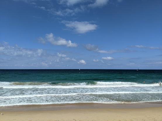 tiny sailing boat on the horizon of the open ocean seen from the beach where turquoise swells roll in