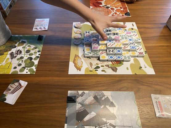 3-Spieler-Spiel Dragon Castle. Eine kleine Hand greift nach den nächsten Steinen aus der zentralen Auslage.