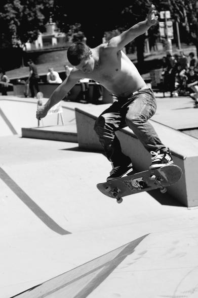 Topless skater guy, doing aerial trick at skate park.  Black and white photo.