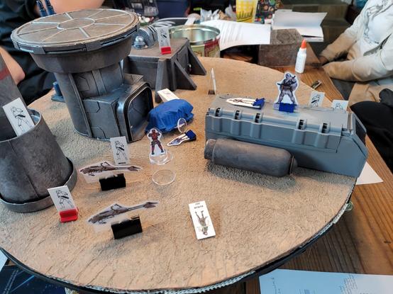 Desert terrain with paper miniatures and futuristic looking buildings and vehicles. (Side view).