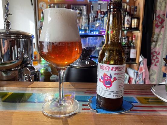 auf der Theke der unmittelBAR stehen ein Bier-Tasting-Glass und eine Flasche India Pale Ale. Im Hintergrund stehen die Flaschen im Glasregal.