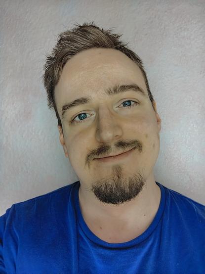 A blue-eyed man smiling in a blue shirt.
