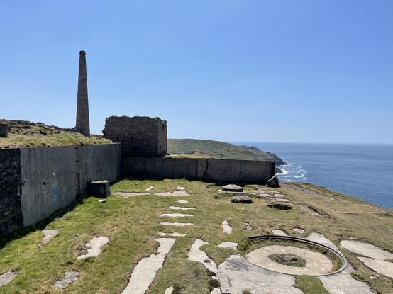Ruins of The Botallack Mine by the cliff, some walls still standing, and a standing chimney still intact