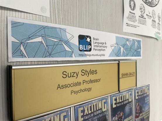 A door sign surrounded by colourful posters: Suzy Styles Associate Professor Psychology ☺️