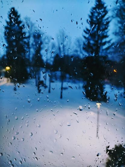 Snowy landscape through drops of rain on a window.