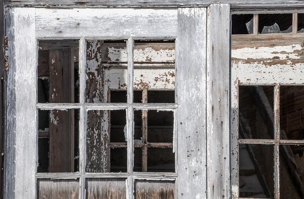 Detail shot of very weathered schoolhouse entrance. The peeling paintwork of the inner door is seen through the window panes of the outer door