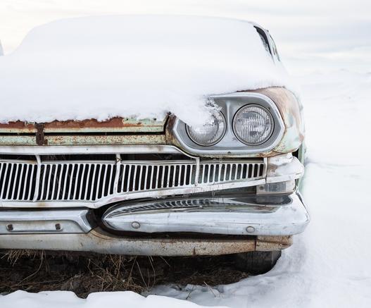Close up view of front of a 1950s Dodge sedan - one half of the front shown - covered in snow and very rusty