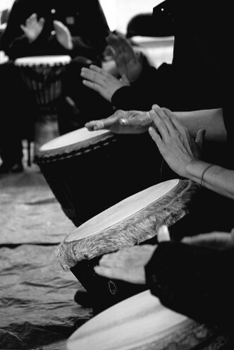 Monochrome photo of multiple people in a hand drumming circle, playing their drums.