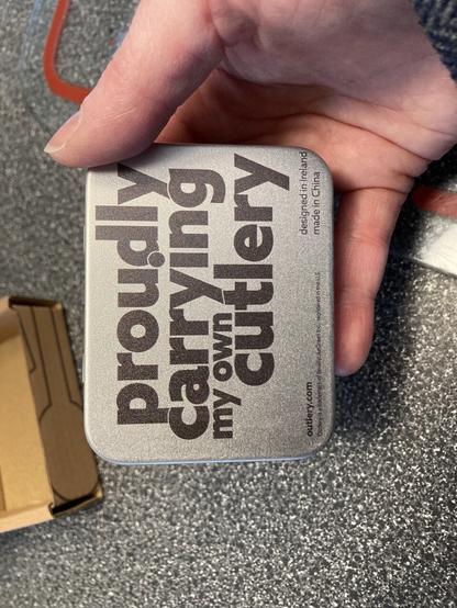 A hand holding a small box that says “proudly carrying my own cutlery”