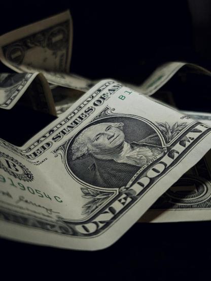 A prominent  somewhat flexed dollar note with several blurred, strongly flexed dollar notes in the background and one below.

Photo by Timis Alexandra on Unsplash.com.