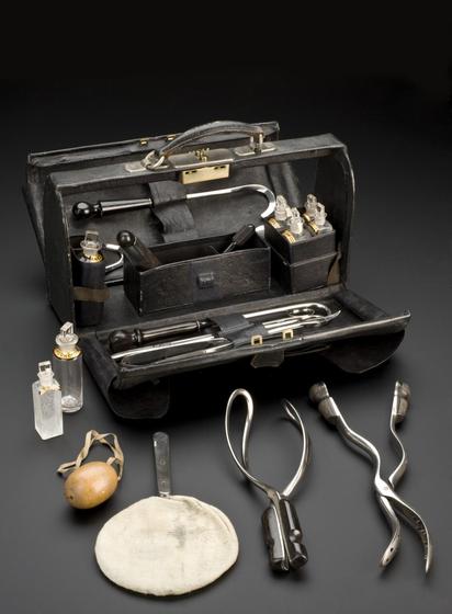 A black leather bag that is open, revealing various midwifery instruments and pharmaceutical bottles.