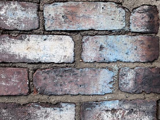 Detail of a brick wall where the individual bricks have discoloured into vibrant shades of silver, blue & purple.