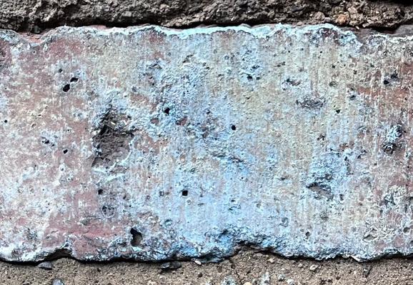 Detail of a single brick, the surface pitted and discoloured into a vibrant turquoise hue.