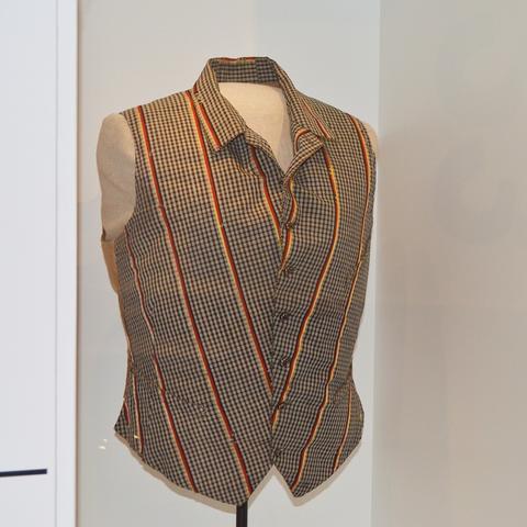 Schwarz-rot-gold-eingefasste Herrenweste von Theodor Reh. Kariertes Leinen mit schwarz-rot-goldenen Streifen, Leihgabe des Regionalmuseum des Geschichts- und Museumsvereins, Alsfeld.
Schwarz-Rot-Gold – die heutigen Nationalfarben Deutschlands werden 1848 während der Märzrevolution als Bundesfarben festgelegt und fassen hier die Weste von Theodor Reh ein. Reh war der letzte Präsident der Frankfurter Nationalversammlung, die 1849 Frankfurter Reichsverfassung verabschiedet und dem preußischen König die Kaiserkrone anbietet.
Die Weste von Theodor Reh ist aktuell in der Ausstellung „Roads not Taken. Oder: Es hätte auch anders kommen können“ im Pei-Bau des DHM zu sehen.