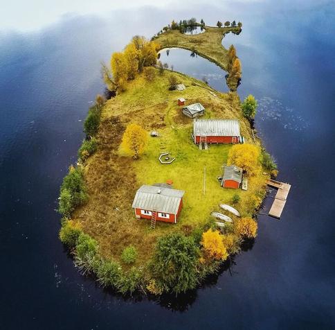 Fall is browning grass and the trees and shrubs are about halfway shifted to a crisp gold. There are three canoes in a row, keels up in the lower left, just below a newish looking L-shaped floating dock.