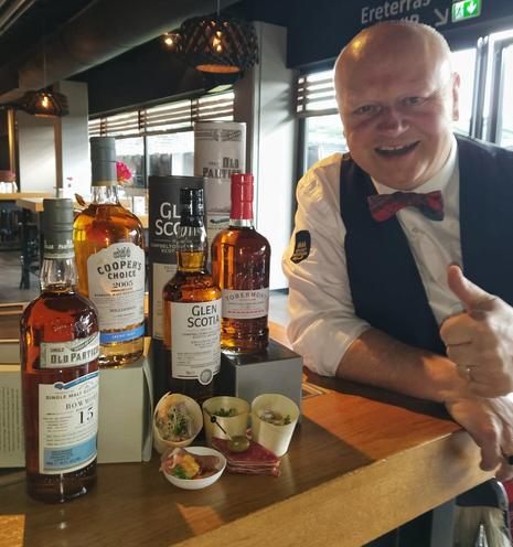 Foto met op de voorgrond vier flessen whisky en rechts whiskyteacher Henri Goossen. De whiskyliefhebbers die het vip-arrangement hadden geboekt kregen vanmiddag deze prachtige line-up voorgeschoteld, met bijpassende hapjes. De Tobermory 21yo single malt Scotch, een rijke fruitige whisky met zowel Bourbon als Oloroso-invloed werd geproefd. Daarnaast proefden de deelnemers The Cooper's Choice Secret Islay 15yo blended malt Scotch, the Old Particular Bowmore 15yo single malt Scotch by Douglas Laing en natuurlijk de festivalbotteling, de Glen Scotia Campbeltown 5yo first fill Oloroso Hogshead.