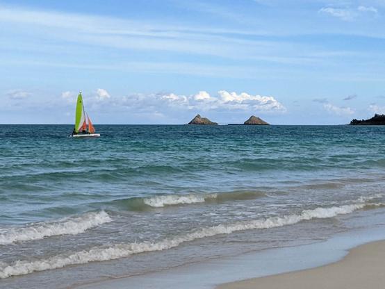 View from the beach of Kailua Bay.  There is a Hobie Cat sailing by, and the Mokolua Islands in the background.