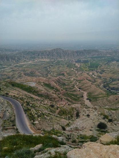 چشم‌اندازی از بالای کوه. تصویر شامل آسمان، کوه، جاده و سبزه است.