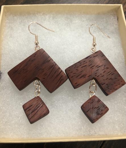 Two handcrafted earrings made out of African Padauk wood with rose gold accessories on a cotton background.

The shape is like a diamond with the bottom point cut out in a square shape and dangling from the rest.