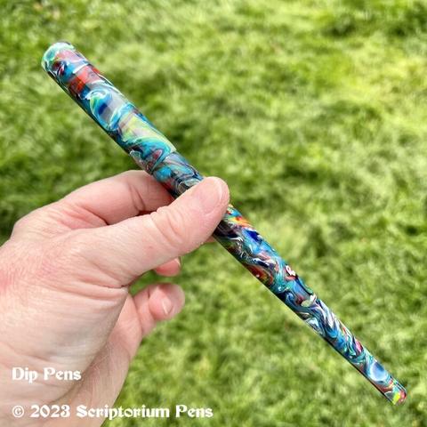 Capped dip pen, held by maker’s hand against a background of green grass.