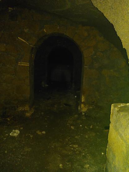 Il fondo di una cantina. Si vede l'arco in tufo e mattoncini che sorregge il soffitto; in fondo, nel buio, se ne intravede un altro. A terra ci sono calcinacci e qualche bottiglia