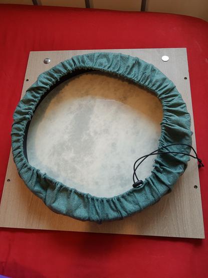 A red surface with a square of worksurface on top.  In the middle is the inside of a frame drum with a green fabric covering secured by elastic drawstring.