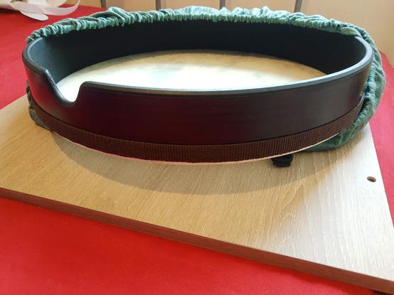 A red surface with a square of worksurface on top.  In the middle is the a frame drum half out of a green fabric covering showing its thumb notch.