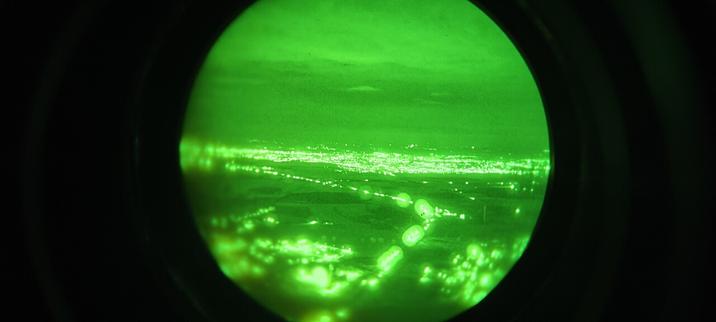 Luftbild durch eine Restlichtverstärkerbrille. Zu sehen ist eine Autobahn und im Hintergrund eine Stadt.