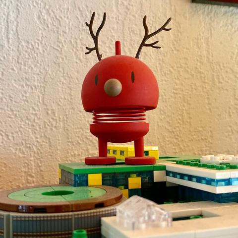 A red hoptimist with antlers. OMG it's a deer! How unique! It's a fun thing though. Standing on top of a model of lego campus.