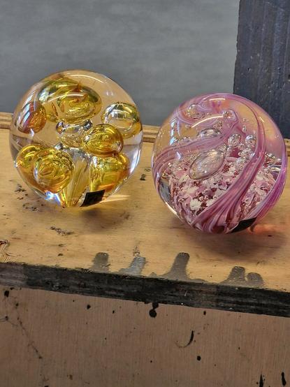 Photo of two paperweights, one with large yellow bubbles in the middle and the other with pink swirls and small bubbles in the middle