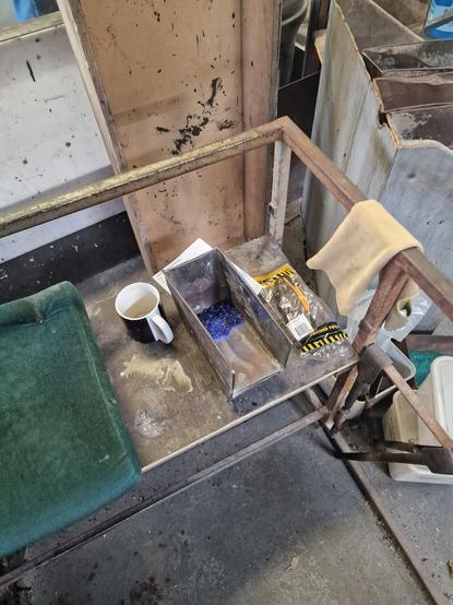 The working space, a padded cushion, metal trays with coloured glass and an empty mug